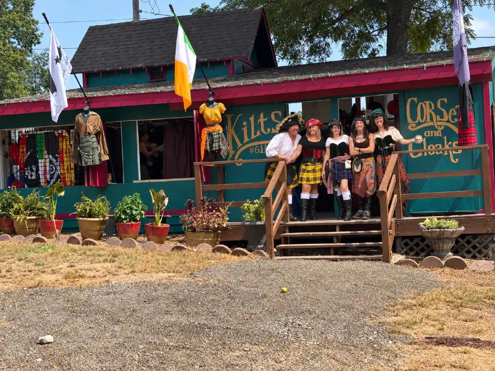 A group outside the Kilt Kountry festival shop, with kilts, corsets, and cloaks on display.